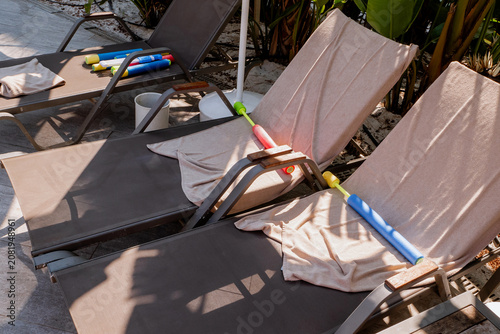 Quadro su tela Empty sun loungers with towels and water blasters under folded beach umbrella, s