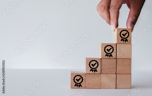 Obraz na plátně Close up of hand placing wooden block with quality guarantee badge icon on top of a staircase