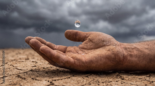 Gritty hand in a desperate gesture catching a falling water drop against a backdrop of parched ground and dark sky