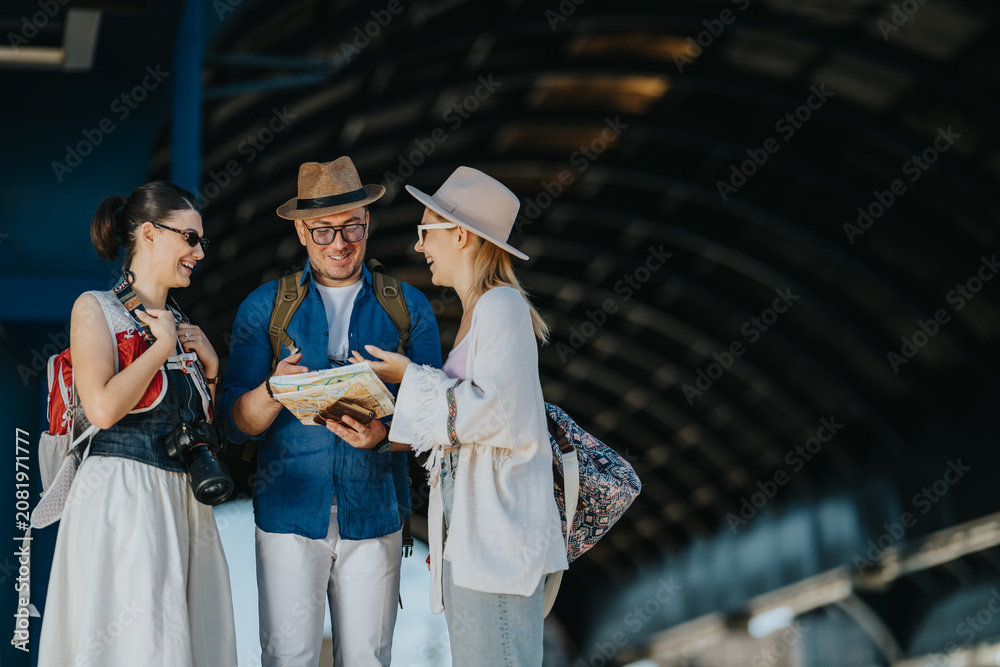 Fototapeta premium Three tourists consult a map while standing together at a station. They smile and plan their route as they prepare to explore.