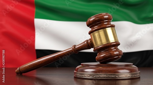 A wooden gavel and sound block resting on a table with the blurred flag of the United Arab Emirates in the background, symbolizing law and justice.