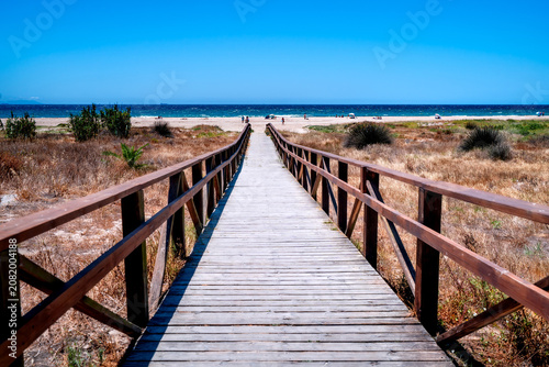 Wooden entrance to Los Lances Beach with people relaxing, Tarifa. Postcard from Costa de la Luz, Spain.