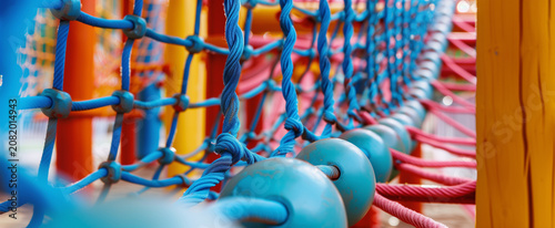 A low angle perspective view of a long climbing bridge path made entirely of blue safety ropes and nets under a clear blue sky at a modern kids playground park