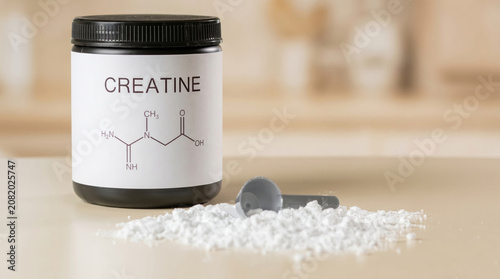Creatine supplement jar with powder and scoop on kitchen countertop  