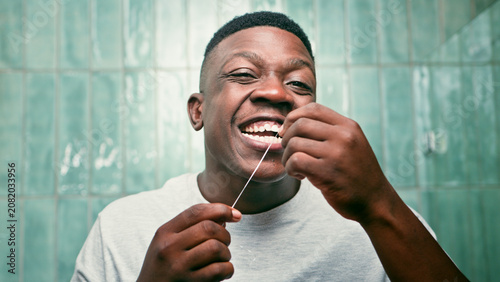 Man Flossing Teeth and Smiling While Practicing Daily Oral Hygiene in Bathroom
