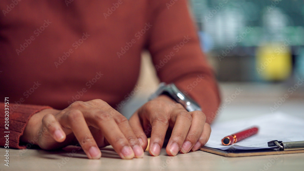 Fototapeta premium Hands rest on a desk with a pen nearby. Person wears a warm-toned sweater and a watch. Fingers are slightly tense, suggesting concentration or thought