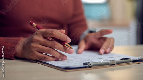 Fotografie Hands hold red pen over clipboard