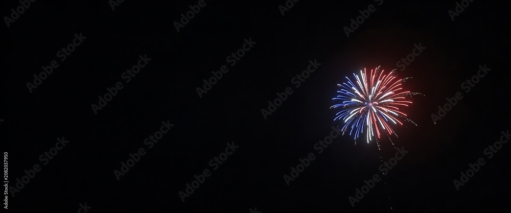 Fototapeta premium Red white and blue patriotic fireworks bursting against a vast black night sky panorama.