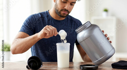 Man measuring protein powder into shaker cup at home kitchen  