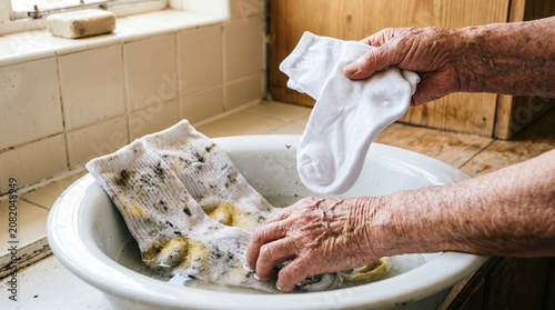 Elderly person washing socks in a bowl with soapy water at home  