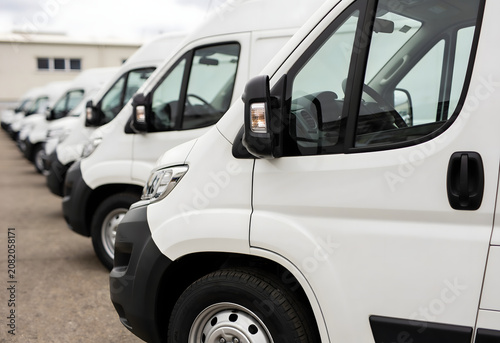 Fleet of White Delivery Vans: A clean fleet of identical white delivery vans is parked in a row, ready for service on a bright, clear day.