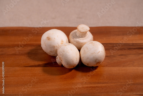 Fresh white button mushrooms (champignon mushrooms) arranged on a wooden cutting board. Natural organic ingredients for healthy cooking, meal preparation, vegetarian recipes.
