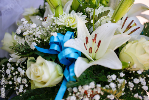 A delicate floral arrangement featuring white lilies, roses, and baby's breath tied with a vivid blue ribbon, conveying grace and charm.