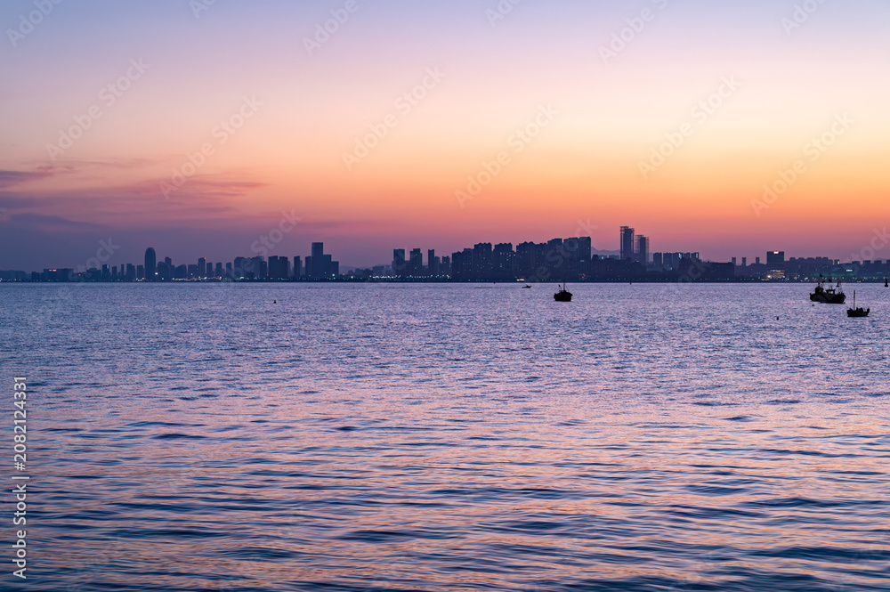 Fototapeta premium Fishing Boats on Sea at Dusk with City Skyline Gradient, Qingdao, China