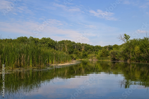 Sunny Summer day landscape of the peaceful Oconomowoc River reflecting a lush wooded landscape beneath a blue sky and wispy clouds near Summit, Wisconsin.