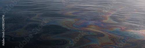 Rainbow oil slick floating on dark water with copy space, website banner, pollution, ecology