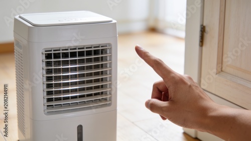 A hand points at a dehumidifier in a room with wooden flooring and a cabinet.