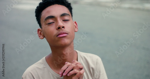 Fotografie Teenage boy with a peaceful expression, eyes closed, hands clasped in a prayerfu