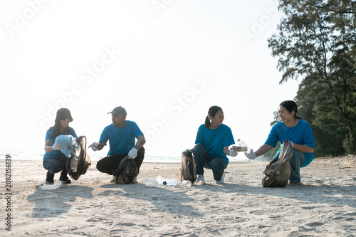 Group of active Asian volunteers cleaning up plastic waste and garbage on the beach together, focusing on environmental conservation and community teamwork.