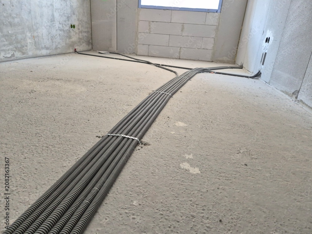 Obraz premium Corrugated plastic electrical pipes laid out and fixed with plastic clamps to the concrete floor grid inside a newly built residential apartment. Underfloor wiring infrastructure and construction phas