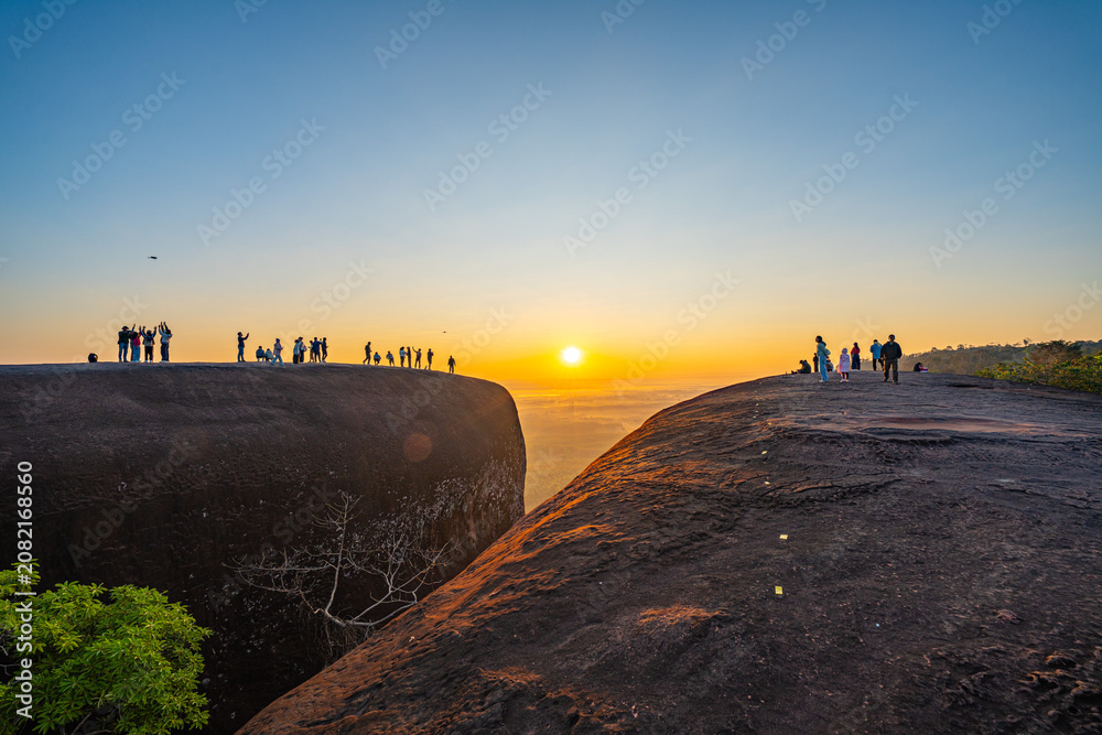 Obraz premium Silhouetted travelers gather on the massive rock formation of Three Whale Rock, watching the first light of day spread across the misty countryside of northeastern Thailand.
