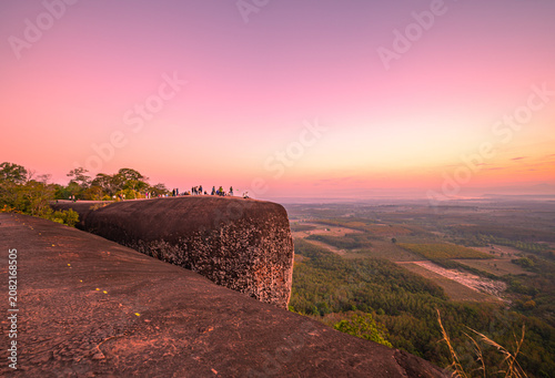 фотографія Epic sunrise at a famous Thai viewpoint, capturing tiny human figures on a colossal rock ledge above a sea of trees, evoking adventure, scale, and serenity