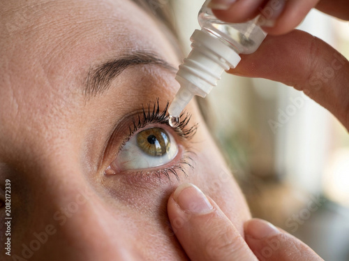 Woman putting medical eye drops into her eye for better vision and relief from dry irritation at home