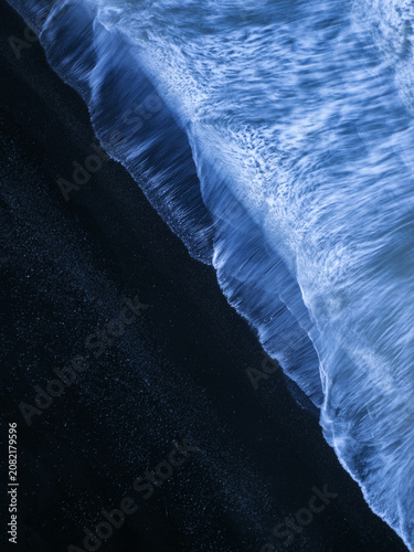 Aerial view of the dramatic black sand beach with white sea foam washing over the dark volcanic shore, Vik, Myrdalshreppur, Iceland.