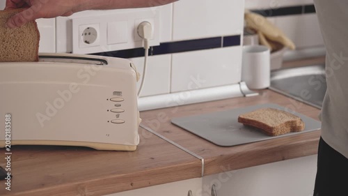 A person places slices of bread into a toaster on a kitchen counter. They then press the lever down to start toasting. This often happens during breakfast preparation.