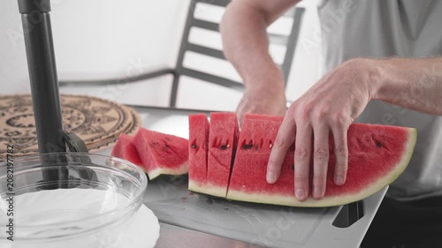 A person cuts a watermelon into neat pieces on a table. The fruit is juicy and red. Fresh slices are ready to be served. The setting is bright and welcoming.