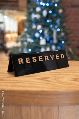 Reserved table sign on a wooden tabletop in a cozy restaurant interior with blurred Christmas tree lights in the background.
