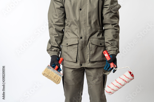 Construction worker in protective clothing holding paint brush and roller, ready for home renovation, decorating or professional painting work.