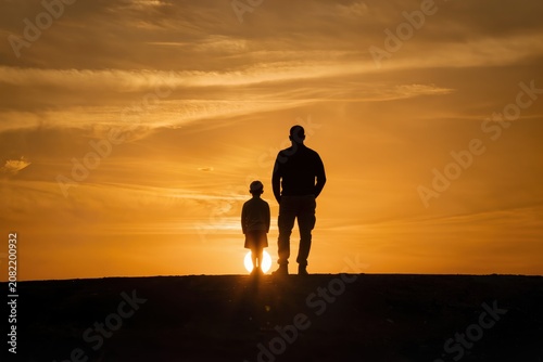 Silhouette d'un père et de son jeune fils se tenant la main au coucher du soleil, symbole de protection et de transmission