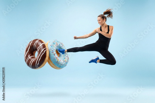Fit Athletic Woman Kicking Giant Donuts in Mid-Air. Healthy Lifestyle vs Junk Food Concept.