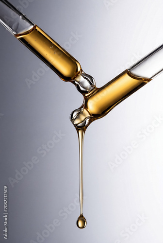 Golden Cosmetic Serum Dripping from Glass Dropper Macro Isolated on Light Background.