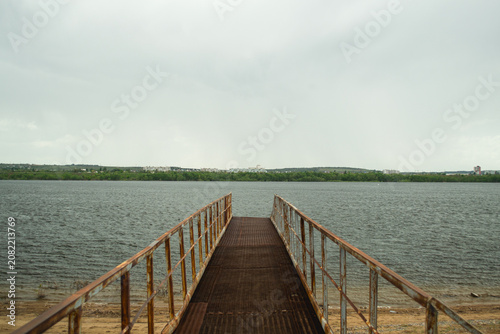 Empty pier leading into calm water under cloudy sky, concept of solitude and direction