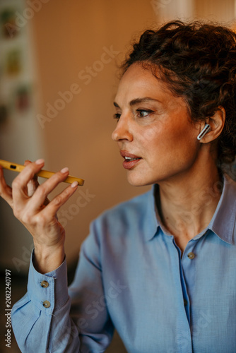 Cuadro en lienzo Woman sending voice message using smartphone and earbud
