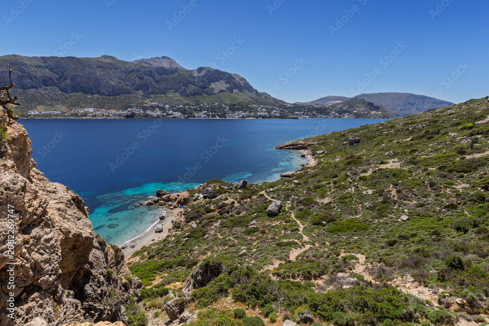 Fototapeta premium Rugged and lush landscape, beaches, coastline and the Aegean Sea on Telendos island in Greece on a sunny day. Mountainous Kalymnos island is in the background.