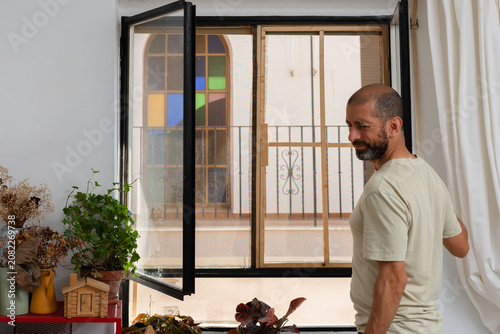 Man opening window and reacting to hot air during summer heatwave at home