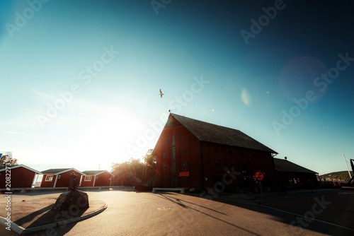 Red scandinavian cabin with white porch under strong sunlight and dramatic shadows.