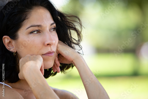 Photos Close-up portrait of a thoughtful young woman resting her chin on her hands while looking into the distance in a green park