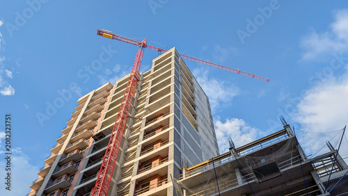 Foto Building with a large red crane on a construction site, workers developing a new