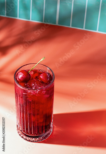 Fotografía Refreshing cherry drink served in a glass with ice on a bright red background du