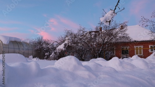 Foto A snow-covered village yard with a brick house and greenhouse is buried in deep snowdrifts