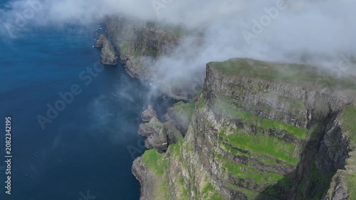 Drone shot of clouds falling down a steep coastal cliff on Suðuroy, Faroe Islands