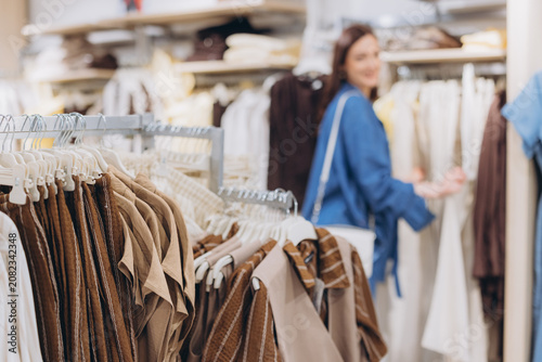 Принти на полотні Young woman shopping for clothes in a retail store, browsing through hangers in