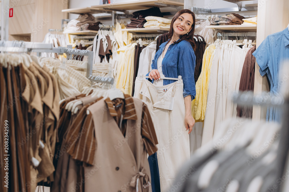 Naklejka premium Woman shopping for clothes in boutique, holding pants, enjoying retail experience and modern fashion trends