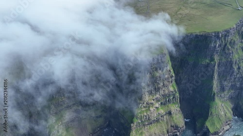 Drone shot of clouds falling down a steep coastal cliff on Suðuroy, Faroe Islands