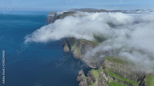 Drone shot of clouds falling down a steep coastal cliff on Suðuroy, Faroe Islands