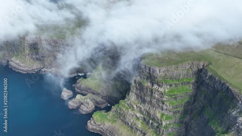 Drone shot of clouds falling down a steep coastal cliff on Suðuroy, Faroe Islands